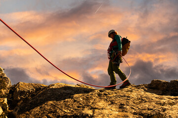 Mountaineer walking across the cliff wearing a helmet. She is wearing a backpack and a helmet. The...