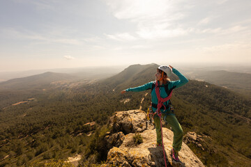 A woman is standing on a mountain top, wearing a blue jacket and a helmet. She is pointing to the...
