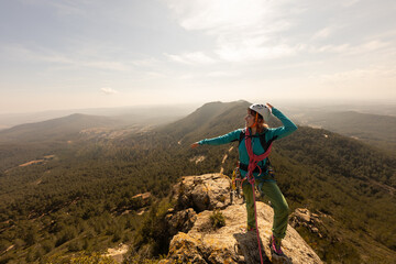 Fototapeta premium A woman is standing on a mountain top, wearing a blue jacket and a helmet. She is pointing to the sky, possibly indicating the direction of a path or a landmark. Concept of adventure and exploration