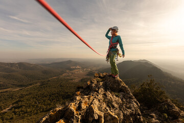 A woman is standing on a mountain top with a rope attached to her. She is wearing a helmet and a...