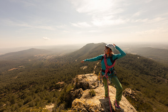 A woman is standing on a mountain top, wearing a blue jacket and a helmet. She is pointing to the sky, possibly indicating the direction of a path or a landmark. Concept of adventure and exploration