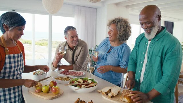 Group of mature friends at home relaxing preparing food for lunch with wine - shot in slow motion