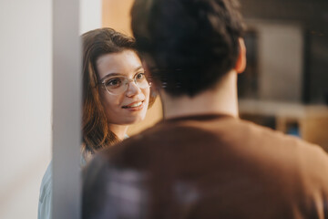 A candid moment as a smiling woman with glasses is seen in the reflection of a mirror, looking at a...