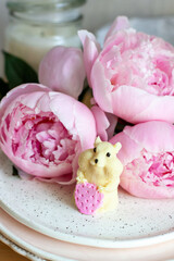 Edible hamster made of white chocolate holding a strawberry. Peonies and candles on the background