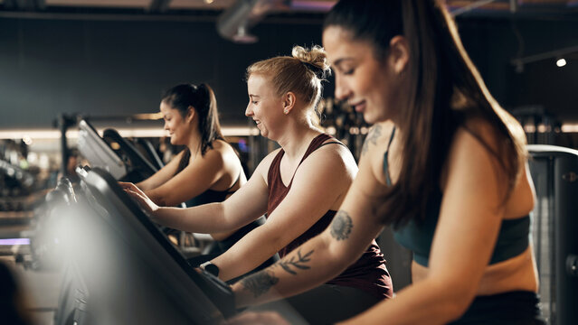 Smiling group of fit young women in sportswear riding on a stationary bikes during a cardio workout session together in a health club