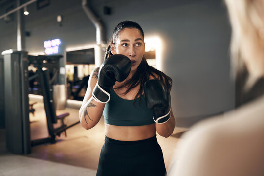 Fit young woman wearing boxing gloves and a tank top practicing punches with a female partner during a self defence workout session together in a gym
