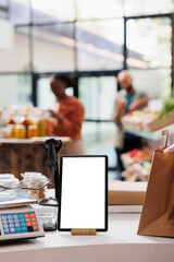 A digital tablet with a blank chromakey mockup template is vertically positioned near glass jars in this image. Smart device with an isolated white screen sits on the counter.