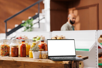 Wireless computer displaying white screen in bio shop filled with freshly harvested fruits and vegetables. Digital laptop showing isolated chromakey mockup template in zero waste store.