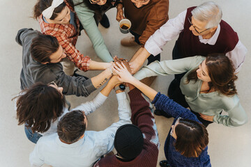 An overhead shot captures a moment of unity as a diverse group of individuals join hands together, symbolizing teamwork and collaboration.