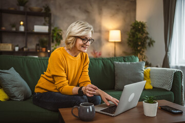 Obraz premium Mature blonde caucasian woman use laptop computer at home for work
