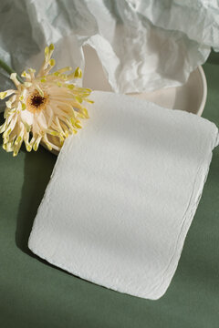 Overhead view of a Blank piece of handmade card on a ceramic plate with gerbera and crumpled paper