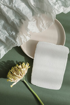 Overhead view of a blank piece of handmade deckle edge card on a ceramic plate with gerbera and crumpled paper