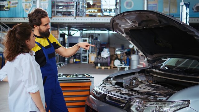 Portrait of smiling african american mechanic in garage using tablet to follow checklist while doing maintenance on customer car. Happy expert in auto repair shop does checkup on vehicle