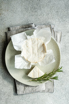 Overhead view of a whole brie with fresh rosemary on a plate and folded napkin