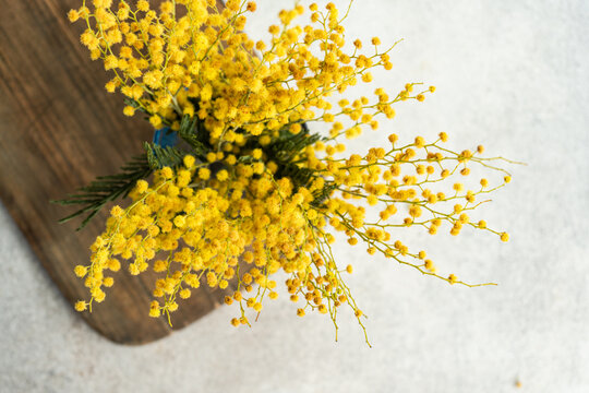 Overhead View Of A Bunch Of Yellow Mimosa Stems In A Vase On A Wooden Chopping Board