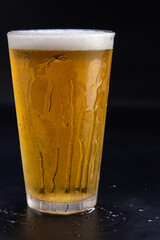 A glass of beer is sitting on a table with condensation on the outside
