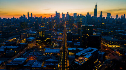 A captivating aerial view of a cityscape at dusk, showcasing illuminated skyscrapers against the darkening sky. The golden hues of sunset paint a serene backdrop, highlighting architectural marvels