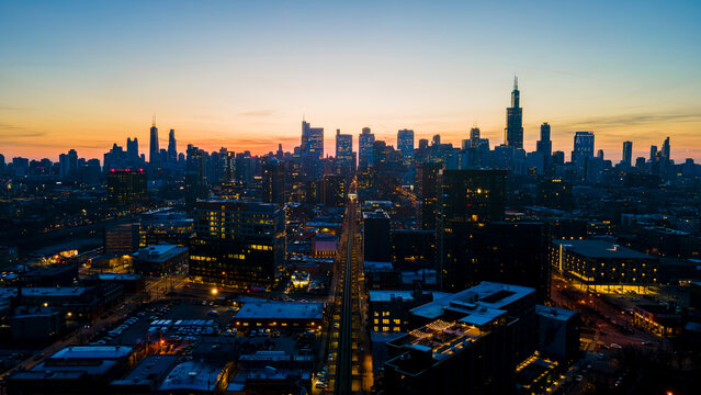 A captivating aerial view of a cityscape at dusk, showcasing illuminated skyscrapers against the darkening sky. The golden hues of sunset paint a serene backdrop, highlighting architectural marvels