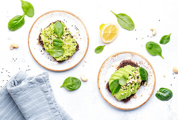 Avocado toasts with spinach and cashew nuts sprinkled with sesame seeds on white table background, top view