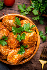 Meatballs with tomato sauce and parsley in bowl on rustic wooden table background. Top view