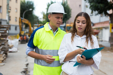 Architect woman and master builder discussing documentation in construction site.