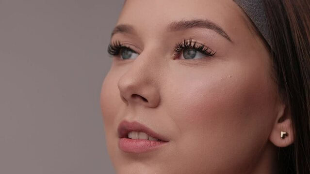 Close up portrait of woman face. Young, beautiful girl with fresh soft skin combing long black eyelashes with special mascara brush. Fake eyelashes. Eyelashes extensions close up.