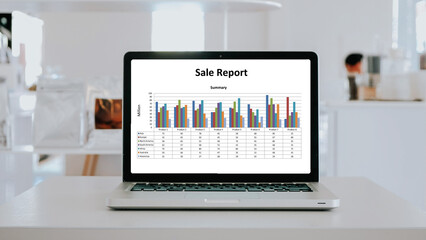 A modern laptop on a white table showcasing a detailed sales report with colorful graphs.