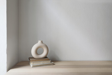 Elegant neutral still life with modern ceramic vase on old books. Wooden table, desk. White wall background. Empty copyspace, no people. Scandinavian, boho home decor. Living room.