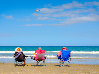 Summer beach seascape with three unidentifiable vacationers relaxing sitting on the beach chairs...
