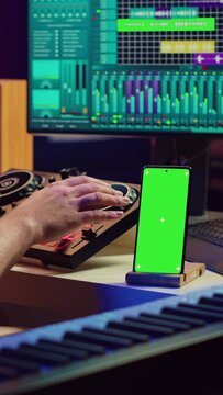 Vertical Video Sound engineer working on mixing and mastering techniques in his home studio, using phone with greenscreen display while he is recording audio. Artist operating soundboard and amplifier