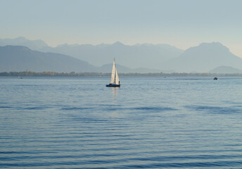 a scenic landscape with a sailing boat on lake Constance by Lindau island with the misty Swiss Alps...
