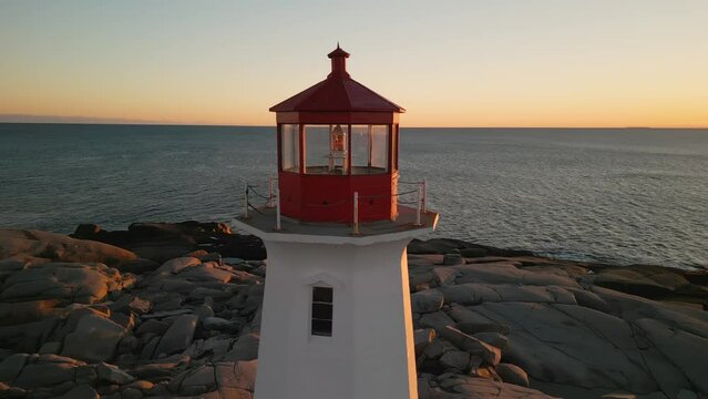 Cinematic drone shot of Peggy's Cove Lighthouse at a beautiful sunset on the Atlantic Coast of Nova Scotia Canada Aerial view. An old lighthouse on a rocky ocean shore with a beautiful evening sunset 