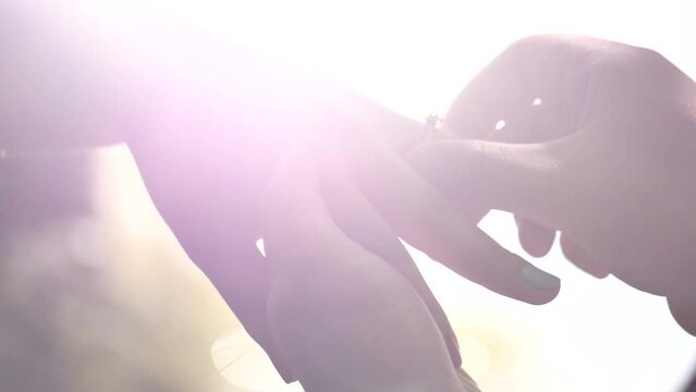 Man, Guy gently holds the hand of his beloved girl and puts the ring on her finger. Marriage proposal. Glare of the sun  close-up
