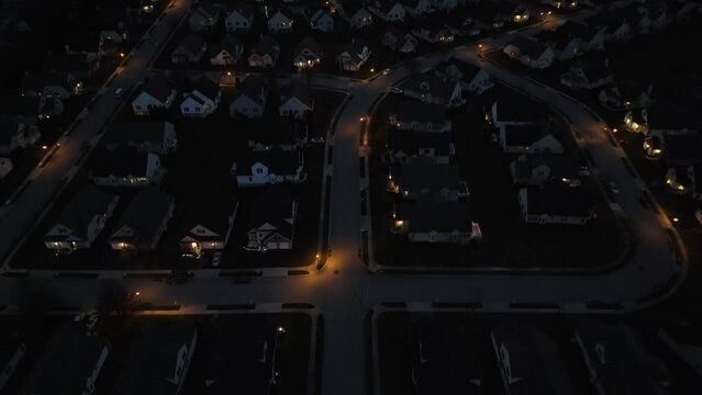 Lights illuminate houses in American neighborhood at night. Aerial descending shot of homes in development at dark.
