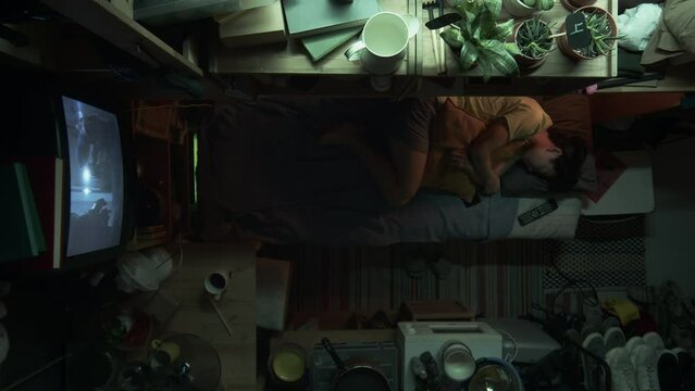 Full top shot of young Chinese woman or man with short hair laying down smartphone, hugging pillow, laying down on bunk bed to sleep, while resting at home in micro apartment