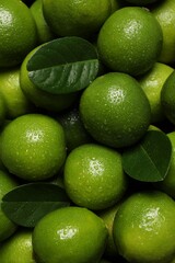 Fresh ripe limes and leaves with water drops as background, top view