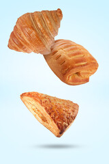 Different tasty puff pastries falling on light blue background