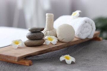 Stacked spa stones, flowers, herbal bags and towel on massage table indoors, closeup