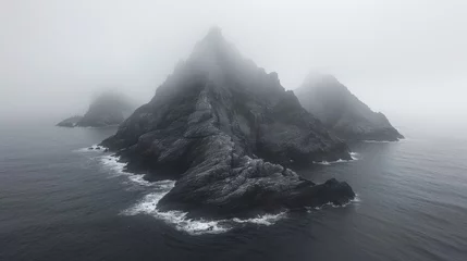Tuinposter Atmospheric black and white photograph of a misty, jagged rock formation rising from the ocean, evoking mystery and the sublime power of nature © Ross