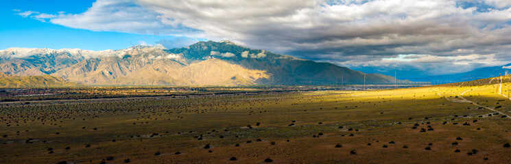 Dappled light from stormy clouds falling on wildflower covered desert hills near Palm Springs