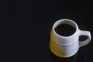 Side view photo of Black coffee in a white and yellow cup on a black ceramic table
