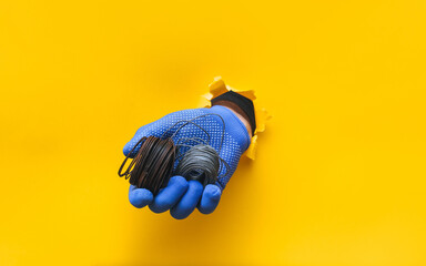 A man's hand in a blue knitted glove holds a coil of steel wire. Torn hole in yellow paper. The...