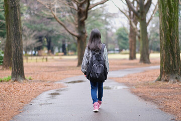 公園の道を歩く小学生の女の子の後ろ姿
