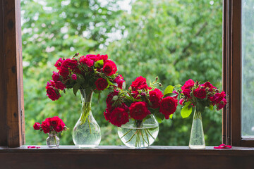 Bouquet of red rose in a vase and a book on a wooden window sill. Still life on the window of an old country house, summer cottage. Floral home decoration.