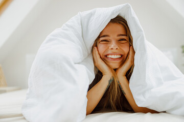 A woman lays in bed under a white blanket, smiling and feeling comfortable