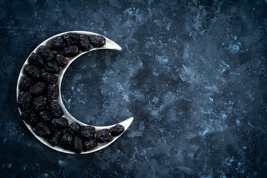 Ramadan iftar food image Dates in a crescent moon shape plate isolated on dark grey texture background, 