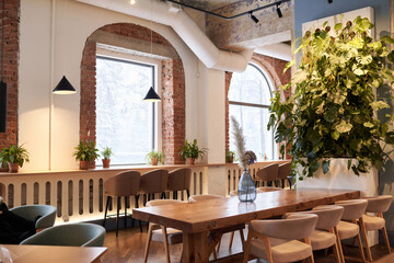 Fototapeta na wymiar No people wide shot of modern upscale restaurant interior with wooden tables, stylish chairs and green houseplants, copy space