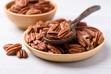 Raw peeled pecan nuts in wooden plate with spoon on white table, Food ingredient
