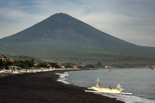 Black sand beach, fishermens, boats and mighty mount Agung volcano at the coast of Amed village, Karangasem, Bali, Indonesia during early morning