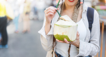 Young adult asian foodie woman backpack traveller eating coconut juice at china town street food.